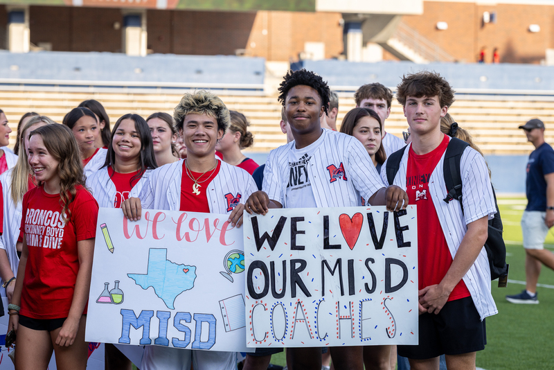 male students holding signs that say we love our coaches and MISD
