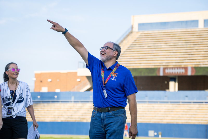 male teacher being introduced and pointing to crowd