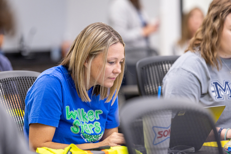 teacher at table peering intently  at computer