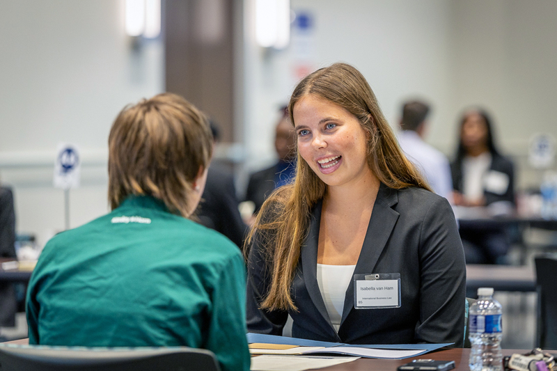 female students talking at a table and one is smiling at the other
