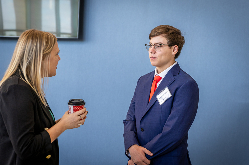 male student in a suit with hands crossed in front of him talks with one of the interviewers befroe the start of the event