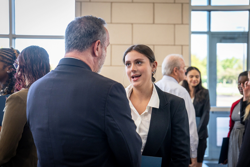 female student in business attire talks with one of the interviewers in the lobby before the beginning of the event