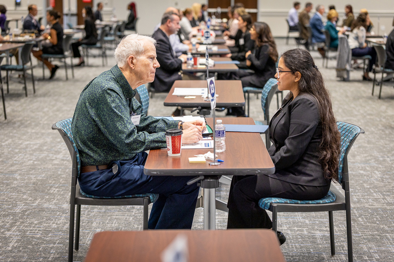female student and business professional seated at a table across from each other and speaking