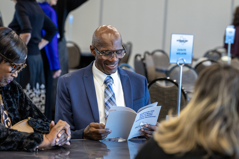 man seated at a table looking at the program and smiling