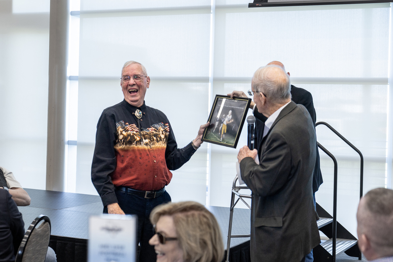 members of the 1958 team laughing as they are presented with an old framed photograph from their season
