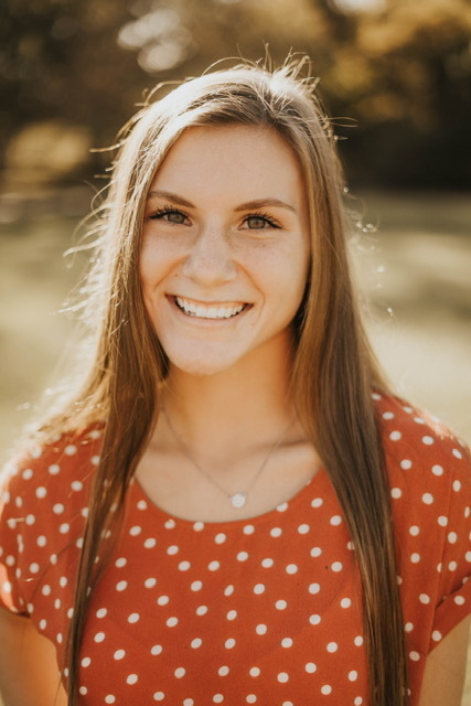 Chloe is wearing an orange shirt with white polka dots. the background is blurred out. 