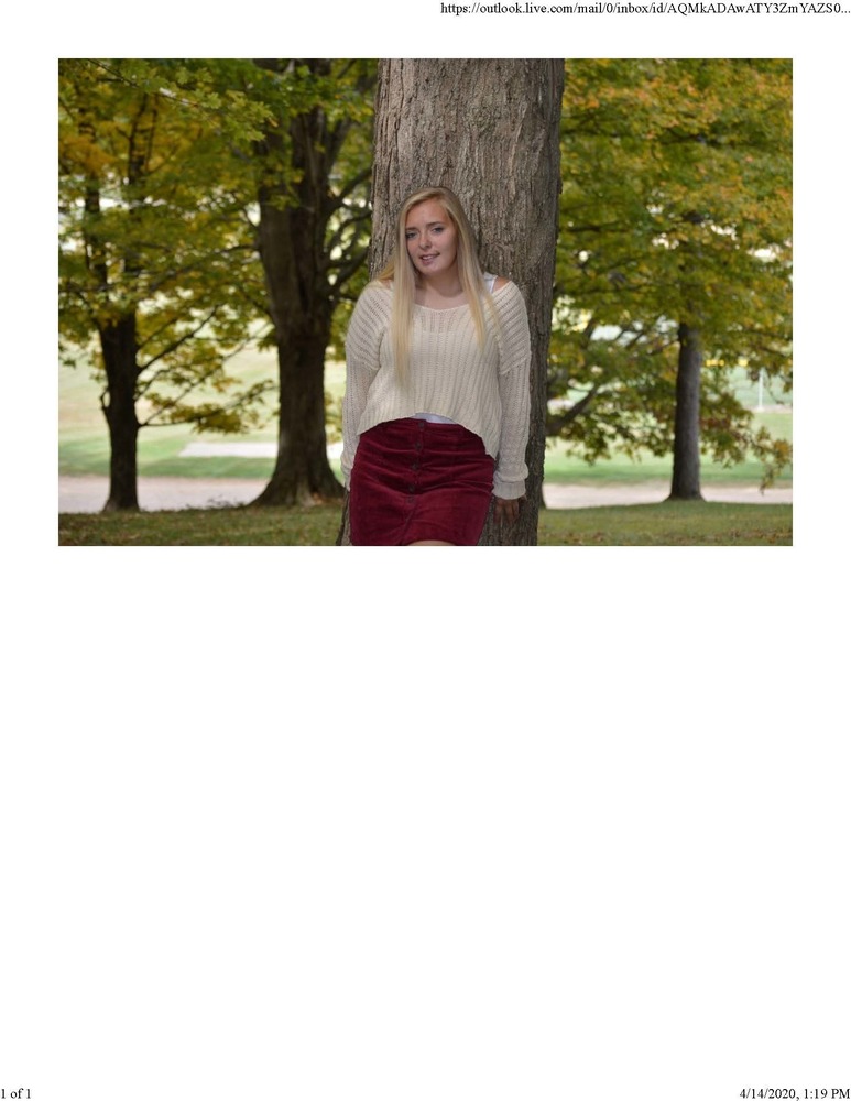 Mackensee is wearing a white/cream sweater with a red skirt. She is standing up against a tree with other trees in the background.