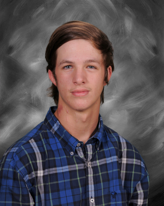 Brennon is wearing a blue/black/grey long sleeve shirt. He is sitting/standing in front of black/grey background