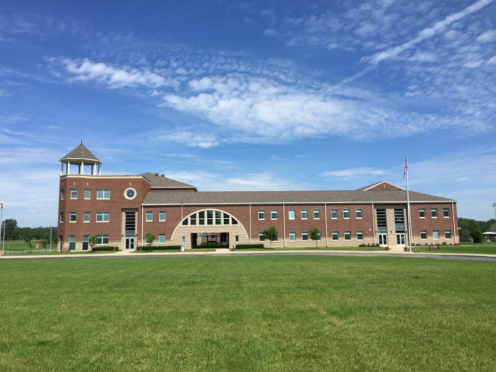 Mechanicsburg Schools, brown building with the American flag to the right of the building. The U drive way and green grass.