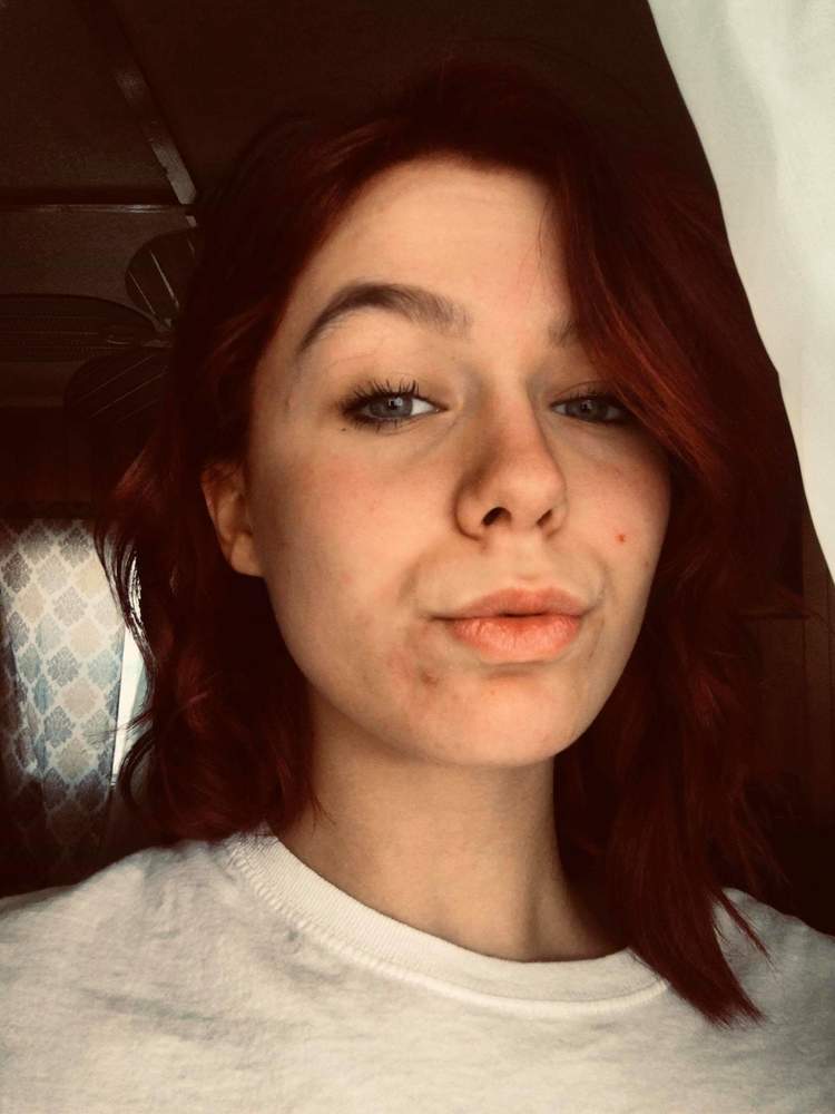 Raven is wearing a white shirt. she is standing or sitting in front of something black/brown.