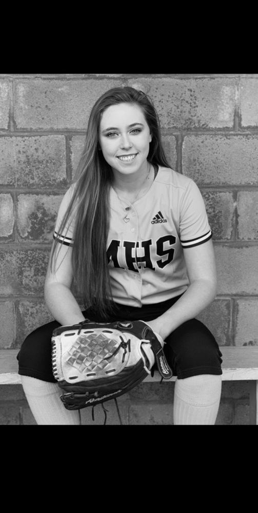Francys picture is done in black and white. She is wearing her softball uniform, holding her glove and sitting on the bench in the dugout.