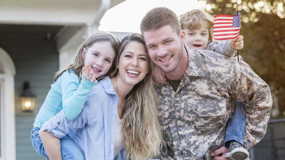 Military family out front of a house and the little boy is holding a flag