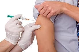 a nurse is wearing white gloves and has a green, yellow and clear needle. They are giving someone a shot in the arm.