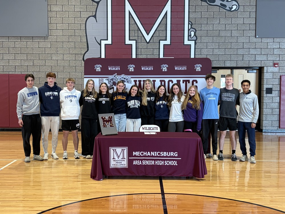 A group of students standing behind a table where they signed their letters of intent.