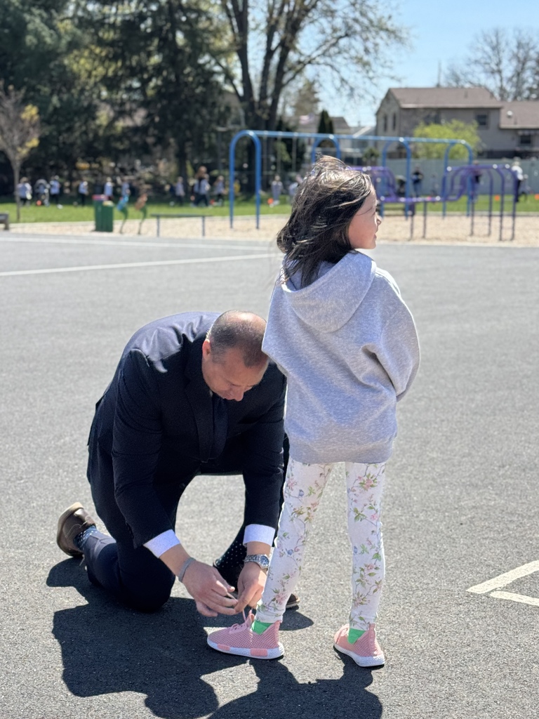 A school principals bends down to tie a young student's shoes.