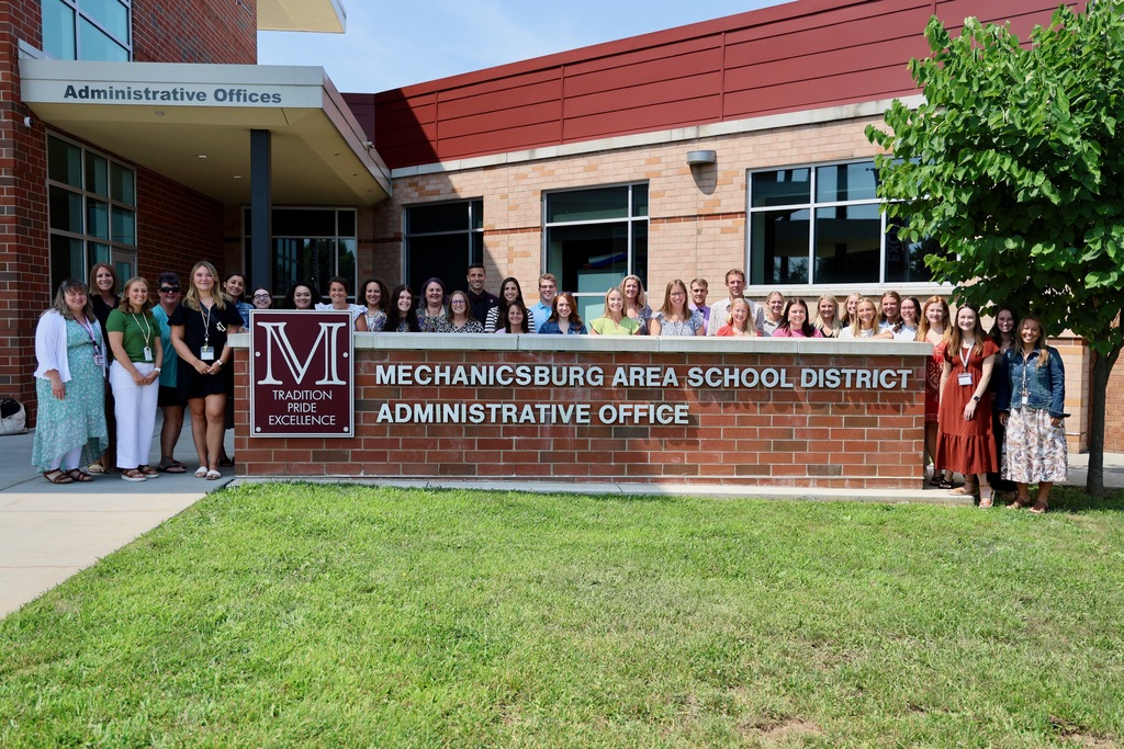 Group of new teachers standing behind an outdoor office sign.