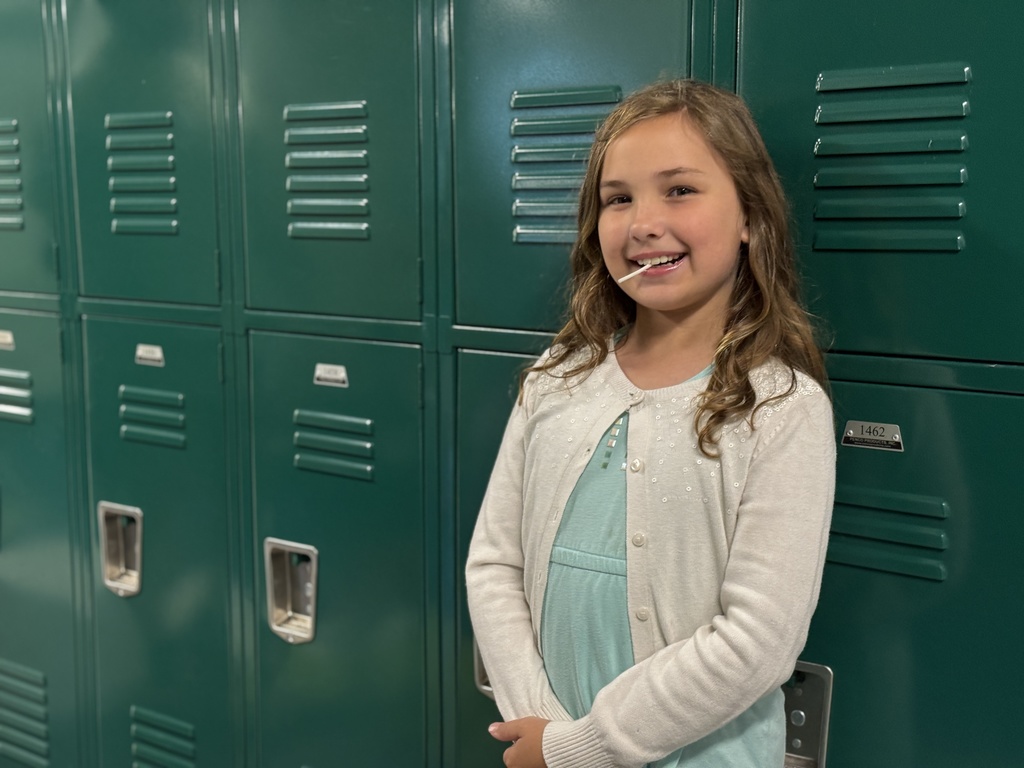 A student standing in front of a row of green lockers.