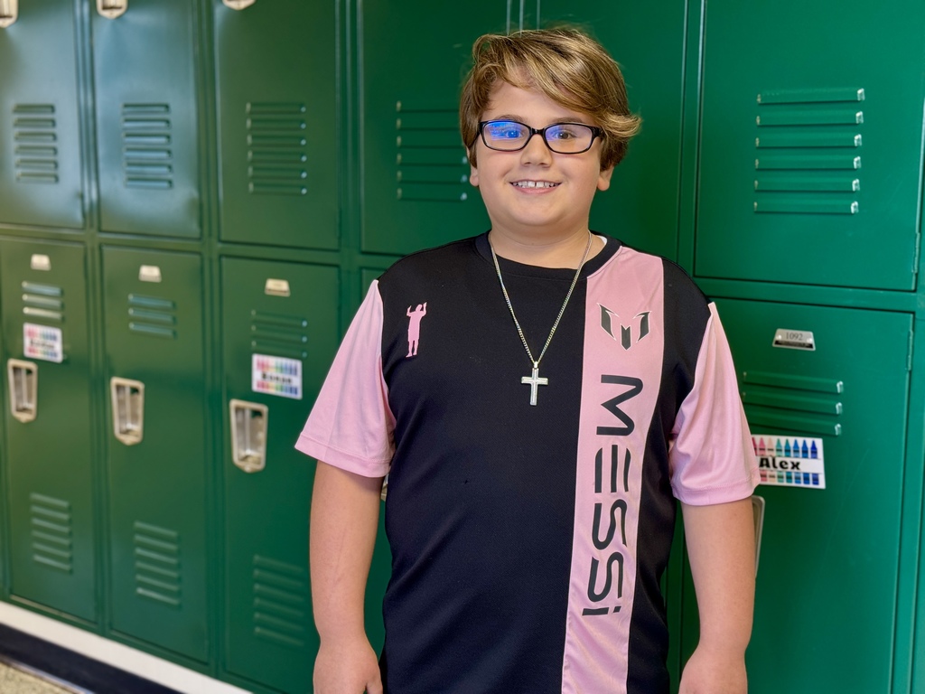 A young student standing in front of a row of green lockers