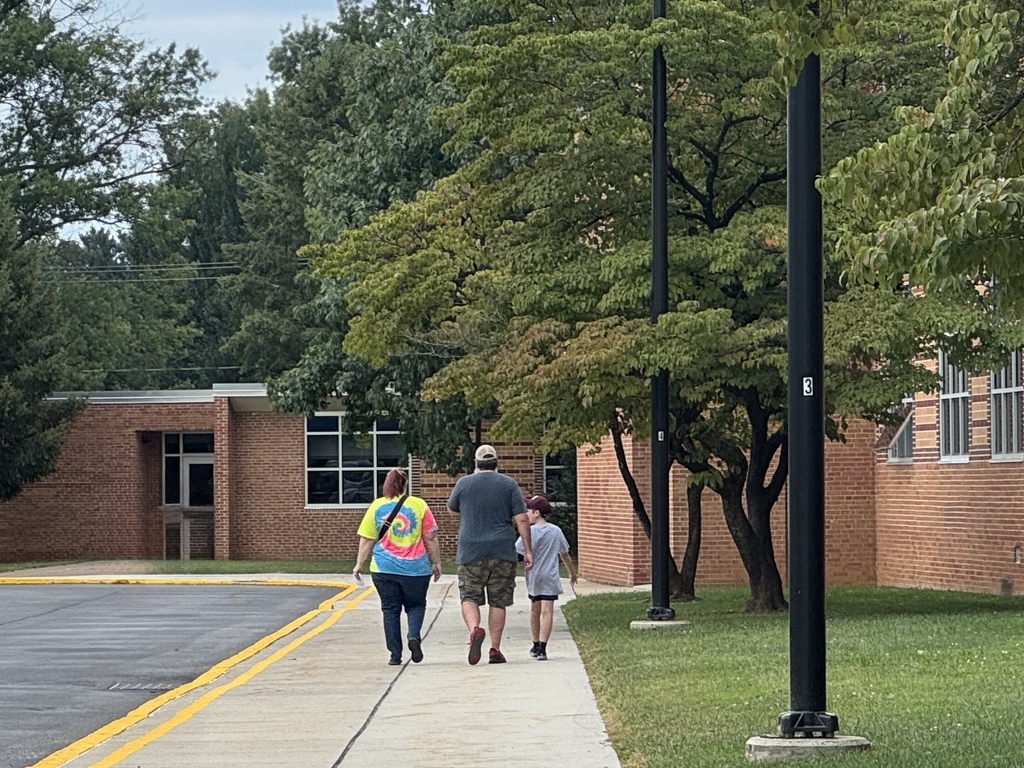 A family walking along the sidewalk in front of a school