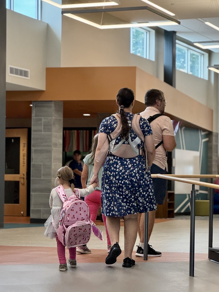 A young student walks a hallway in a school with adults.