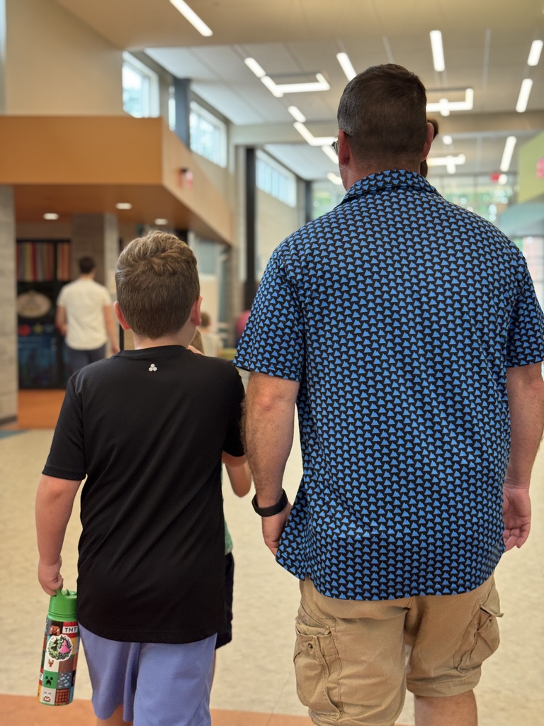 A young student walks a hallway in a school with an adult