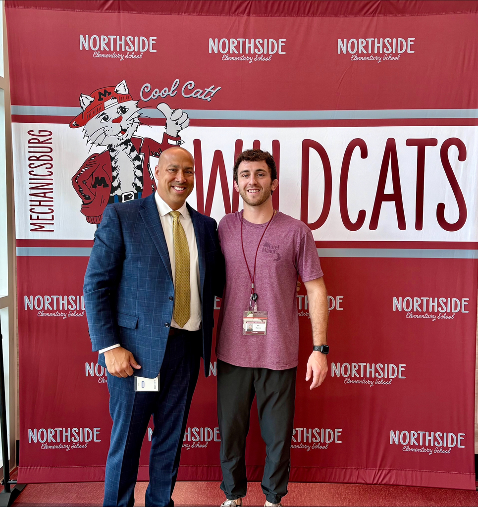 Two male educators standing in front of a maroon Wildcats banner