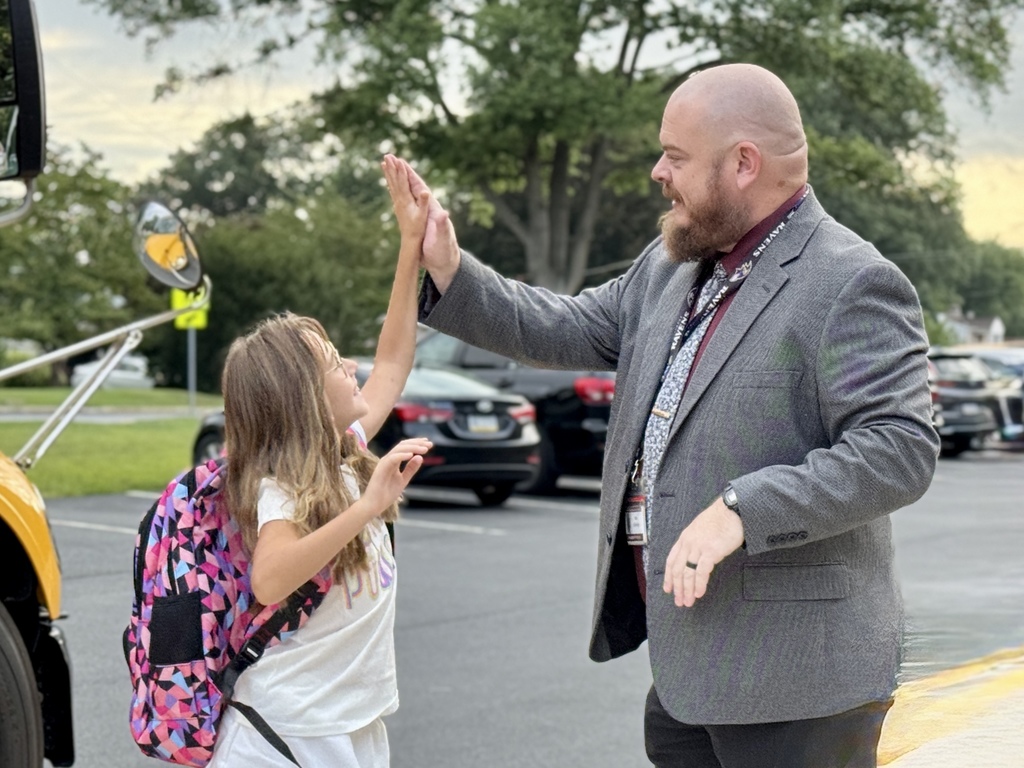 A principal giving a high five to a student as she gets off the bus