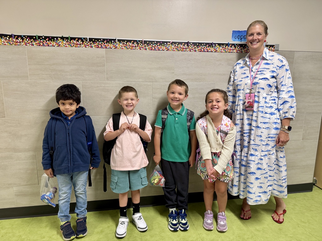 Group of young students smiling and standing beside their teacher on the first day of school