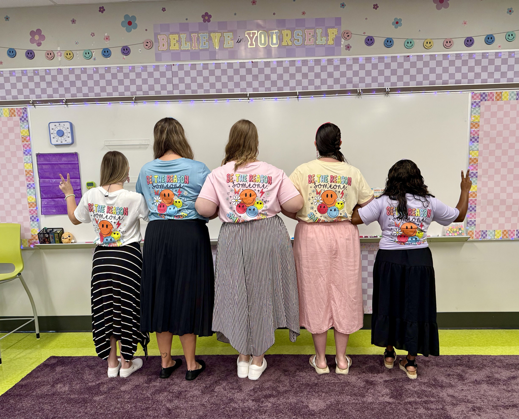 A group of teachers showing the back of their shirts that say  Be The Reason Someone Smiles Today