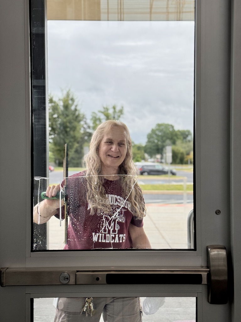 Photo through a window of a custodian cleaning the windows on a door.