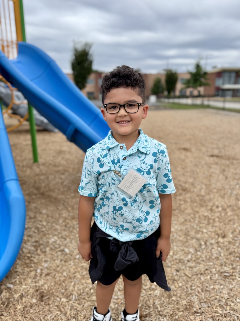 Young boy smiling on a playground. There is a blue slide behind him.