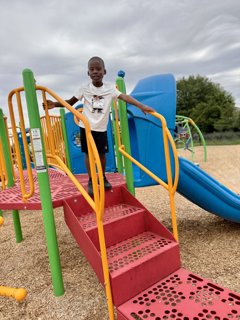 Young boy standing on steps that lead up to a playground slide