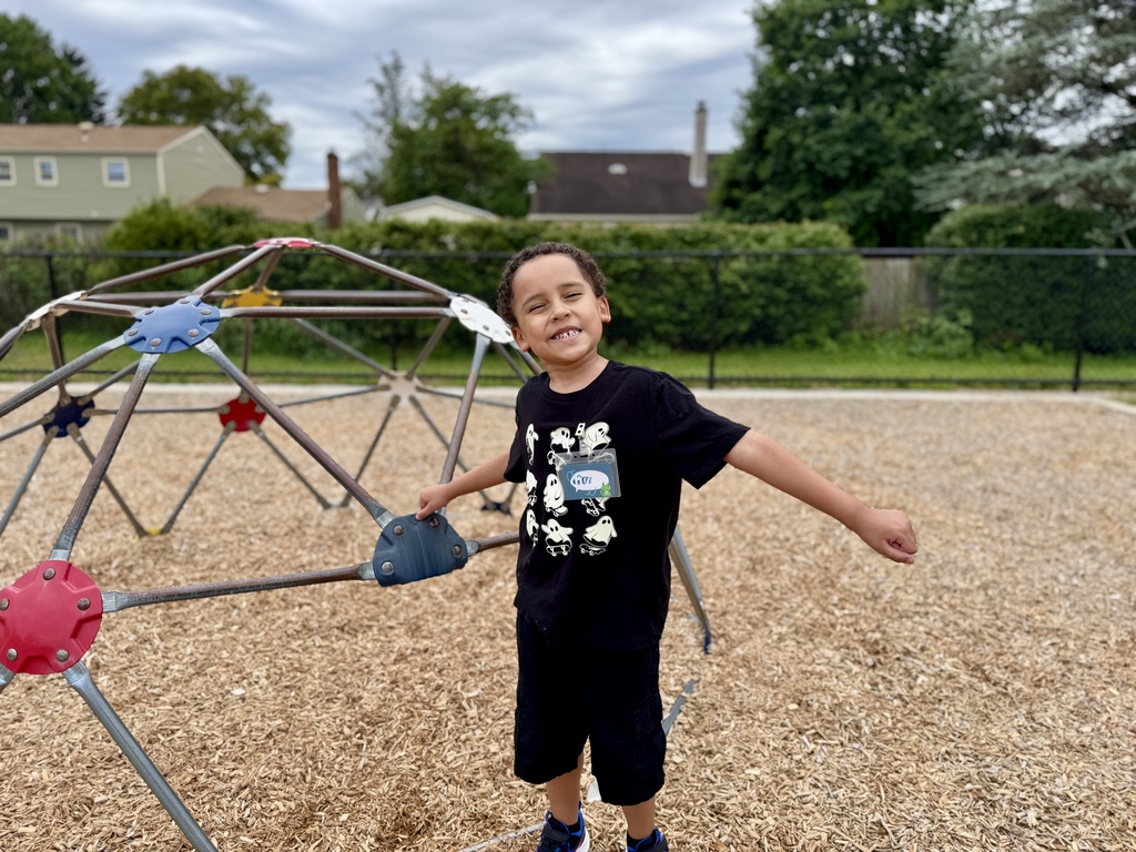 Boy smiling, arms wide open as he stands on a school playground