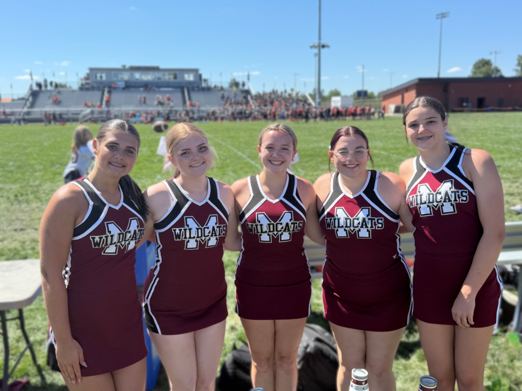 A group of cheerleaders standing in front of a football fieldt