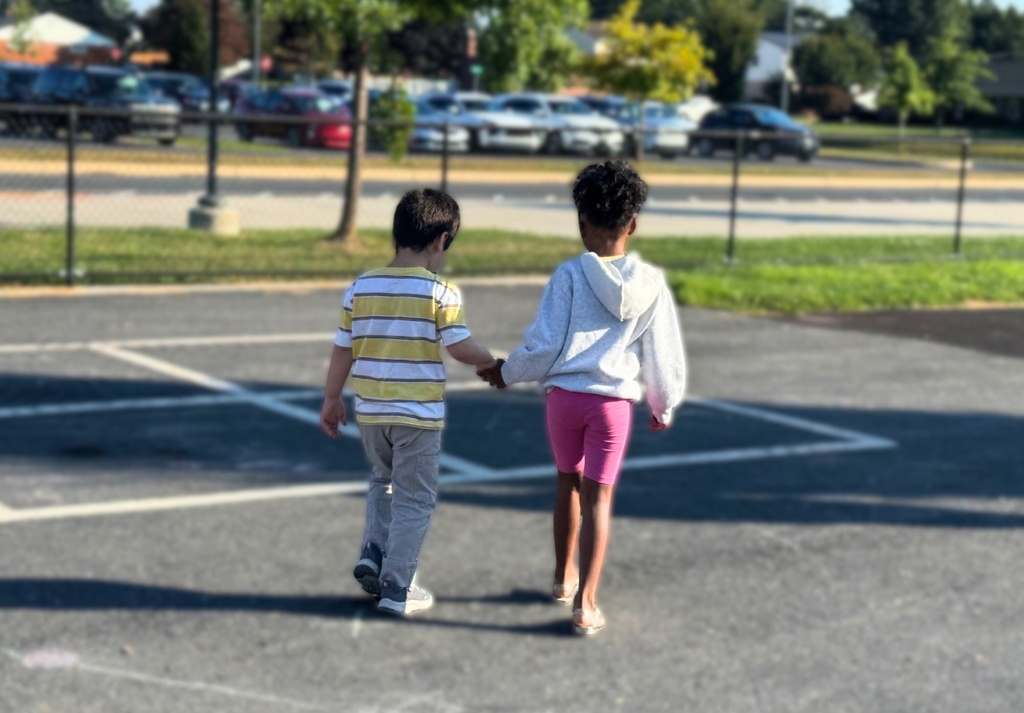 Two young students walking across the parking lot holding hands.