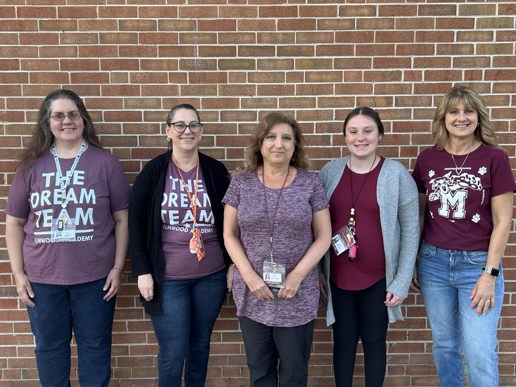 Group of staff standing in front of a brick wall and all wearing maroon.