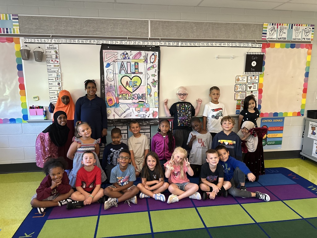 Students sitting on the floor in front of a poster they designed that says All Are Welcome.