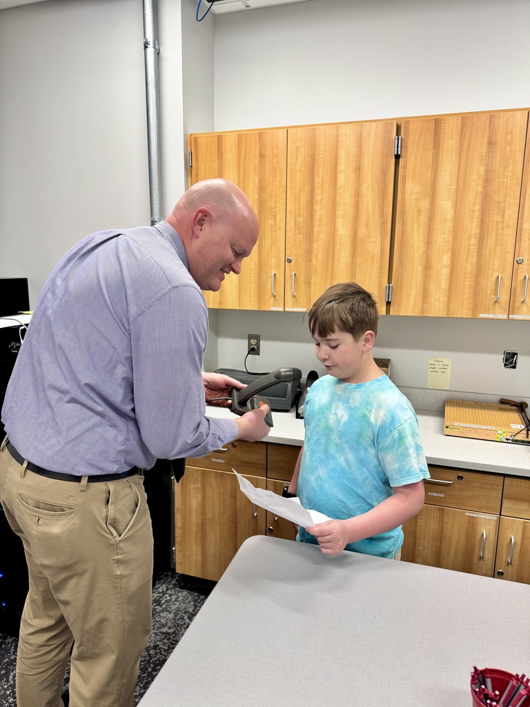 A school principal hold a microphone while a young student reads the morning announcements.