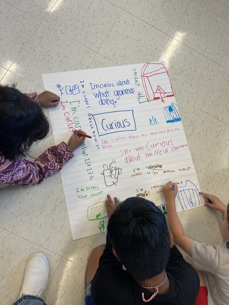 Students laying on the floor to write on large pieces of chart paper.