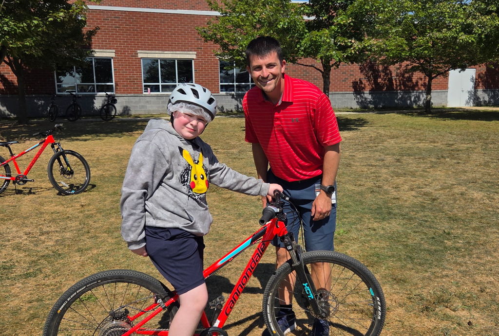 A teacher standing beside a student on a bicycle during phys ed class.
