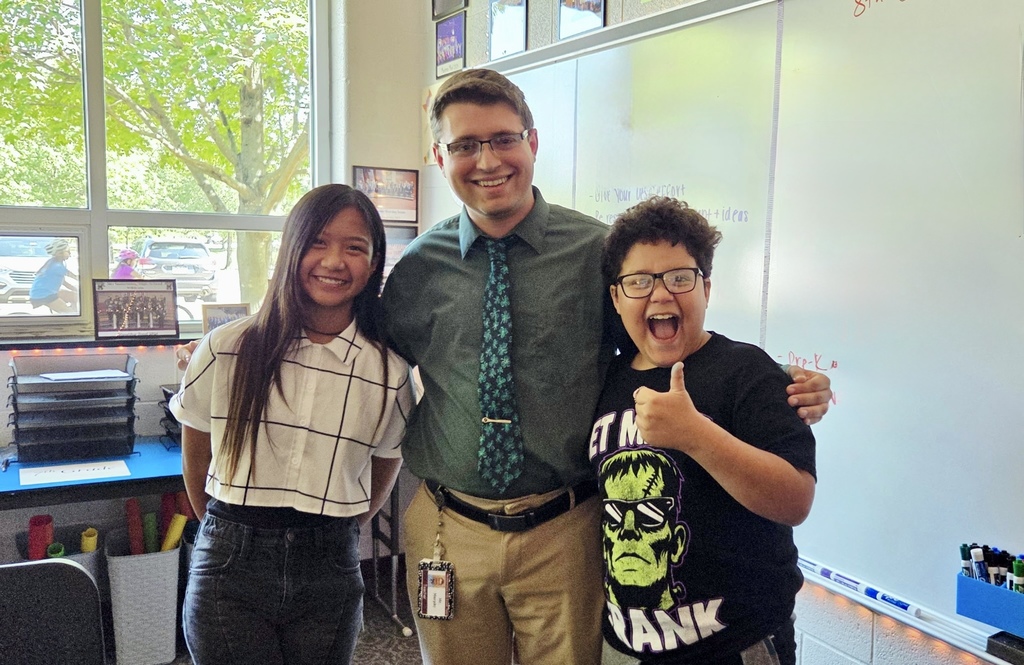 A teacher standing between two students in class. Lots of smiles!