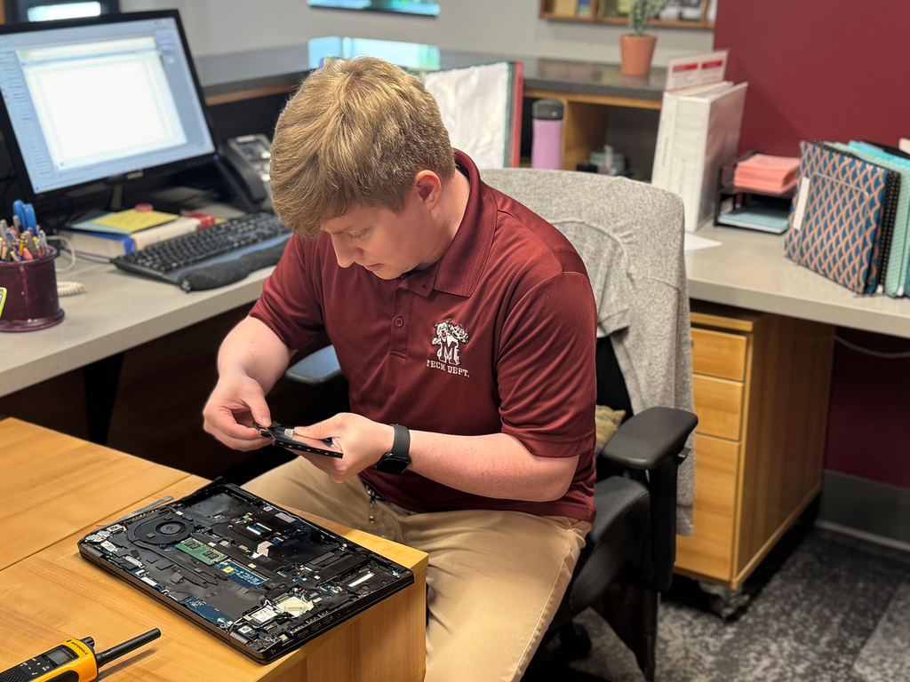 A technician sits at a desk to repair a laptop.