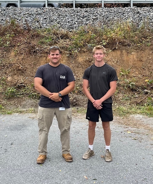 Two maintenance workers standing beside each other, hands crossed in front of them.