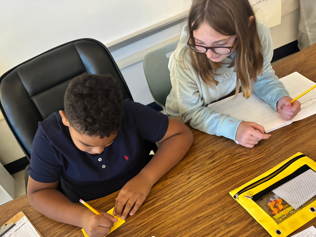 Students writing on notecards and notebooks while sitting at a desk
