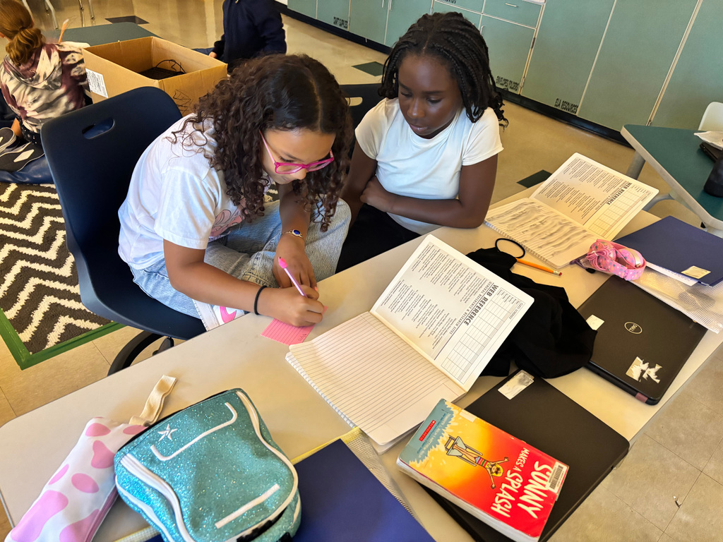 Students sitting at a desk writing on notecards