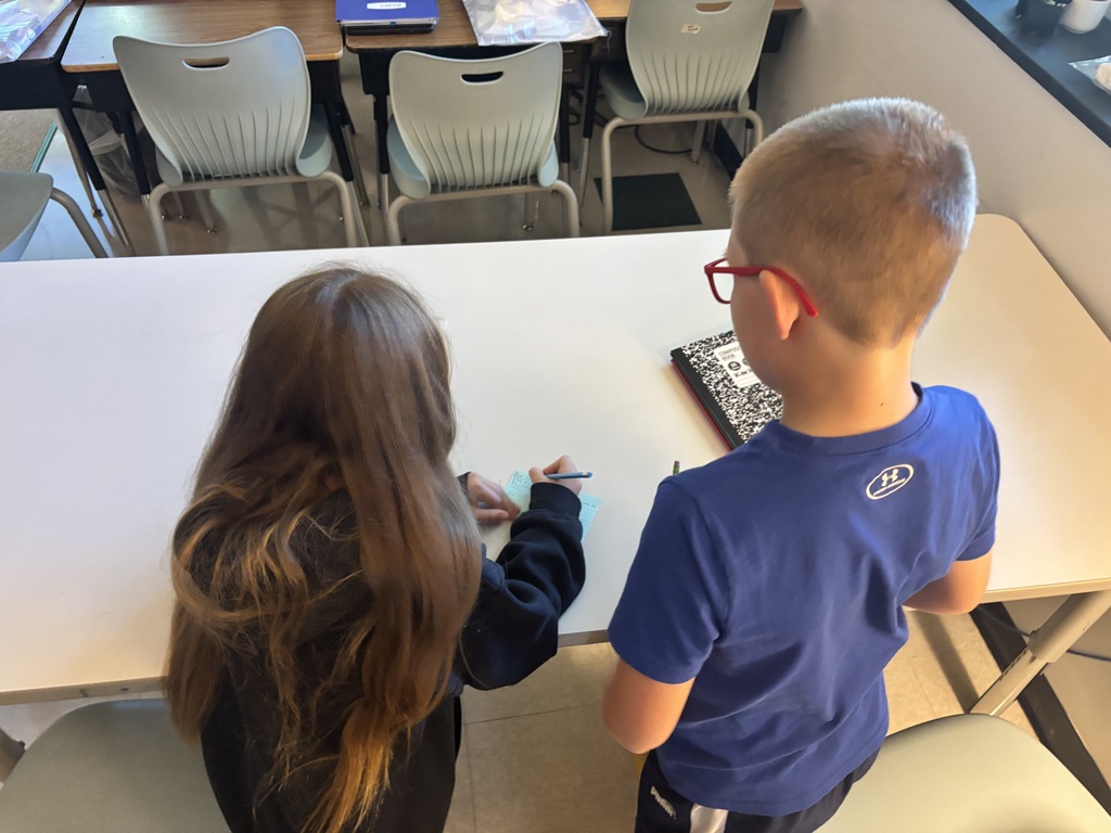 Students writing on notecards while standing at a table
