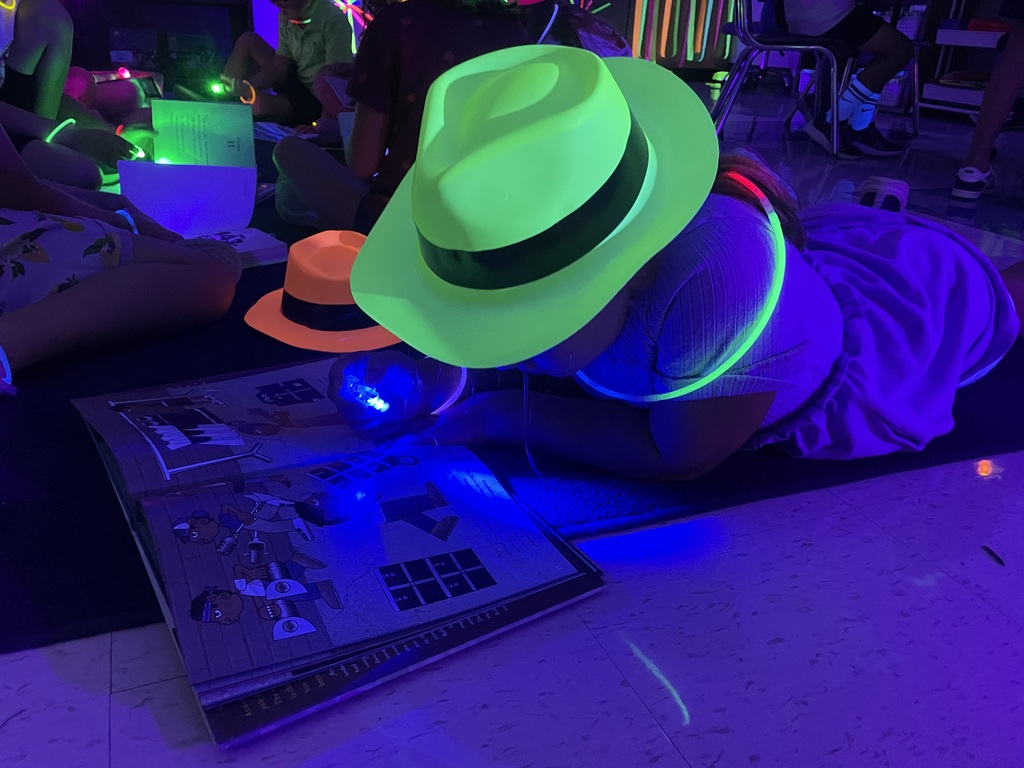 Student laying on the floor reading with glow in the dark finger lights