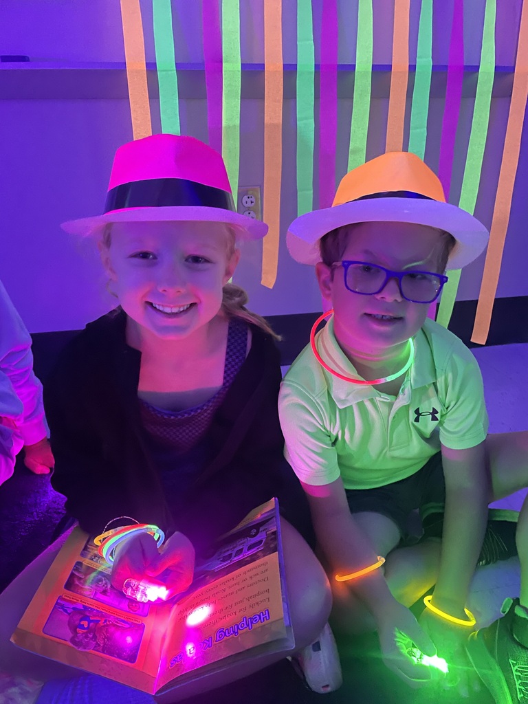 Students on the floor reading with glow in the dark finger lights