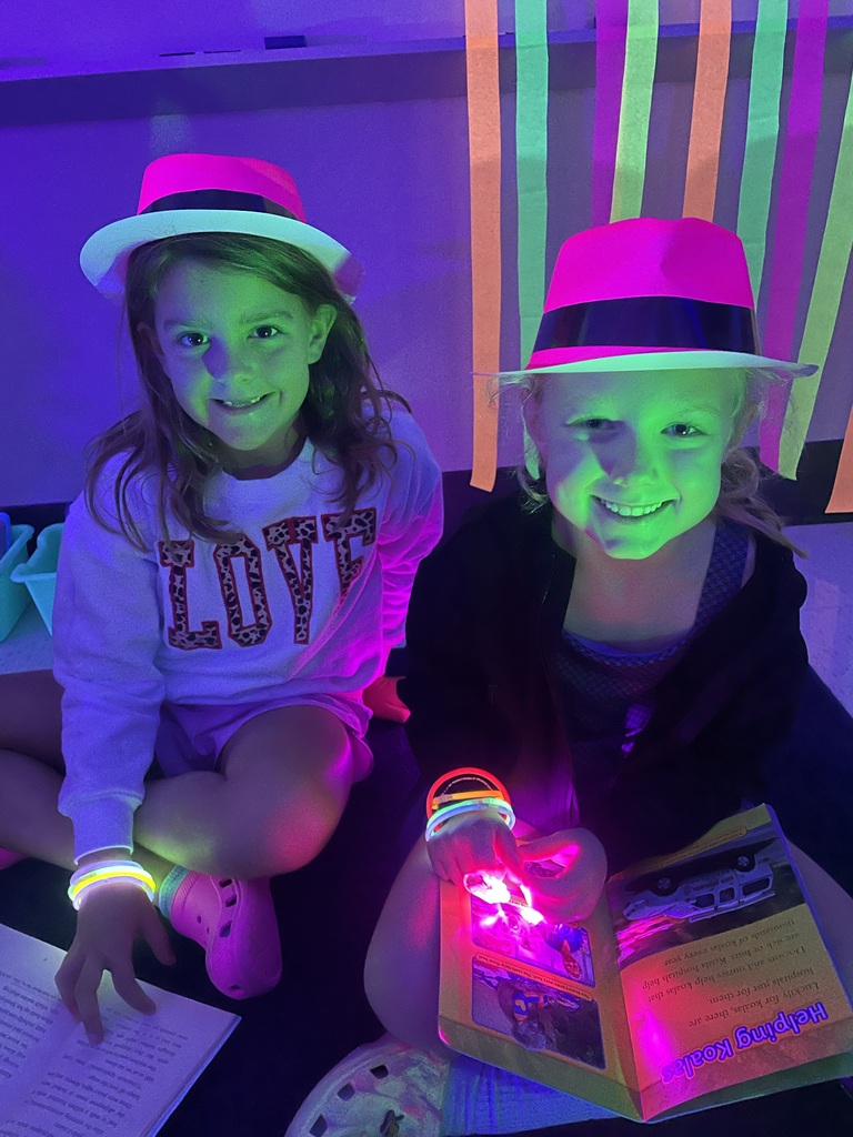 Students on the floor reading with glow in the dark finger lights