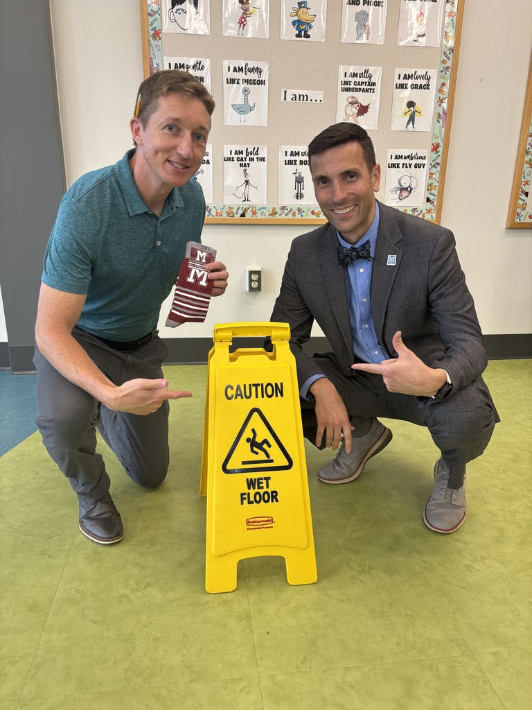 Two adult educators kneeling beside a Caution, Wet Floor sign.